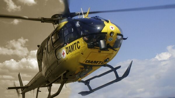 ÖAMTC Hubschrauber im Flug. Im Hintergrund Himmel mit Wolken. Die linke Hälfte des Bildes ist in Schwarz-Weiß ist.