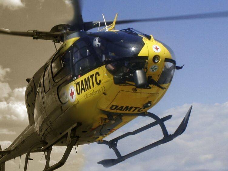 ÖAMTC Hubschrauber im Flug. Im Hintergrund Himmel mit Wolken. Die linke Hälfte des Bildes ist in Schwarz-Weiß ist.