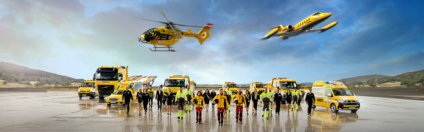 Eine Flotte von gelben Rettungsfahrzeugen und Luftfahrzeugen steht auf einem Flugfeld. Zu sehen ein Krankenwagen, ÖAMTC Pannenfahrzeuge, ein Abschlepp-LKW, ein Rettungshubschrauber in der Luft sowie ein Ambulanzflugzeug. Davor stehen Einsatzkräfte in leuchtender Schutzkleidung. 