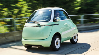 Das hellgrüne Kleinfahrzeug Microlino fährt durch einen Kreisverkehr.