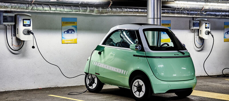 Das Kleinfahrzeug Microlino in hellgrün steht an einer Ladestation angesteckt in einer Garage.
