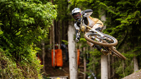 Mountainbike-Profi Vali Höll im Sprung auf einer Downhill-Strecke im Wald.
