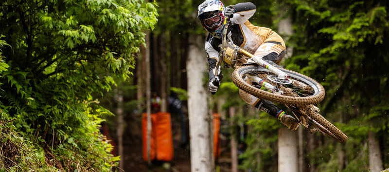 Mountainbike-Profi Vali Höll im Sprung auf einer Downhill-Strecke im Wald.