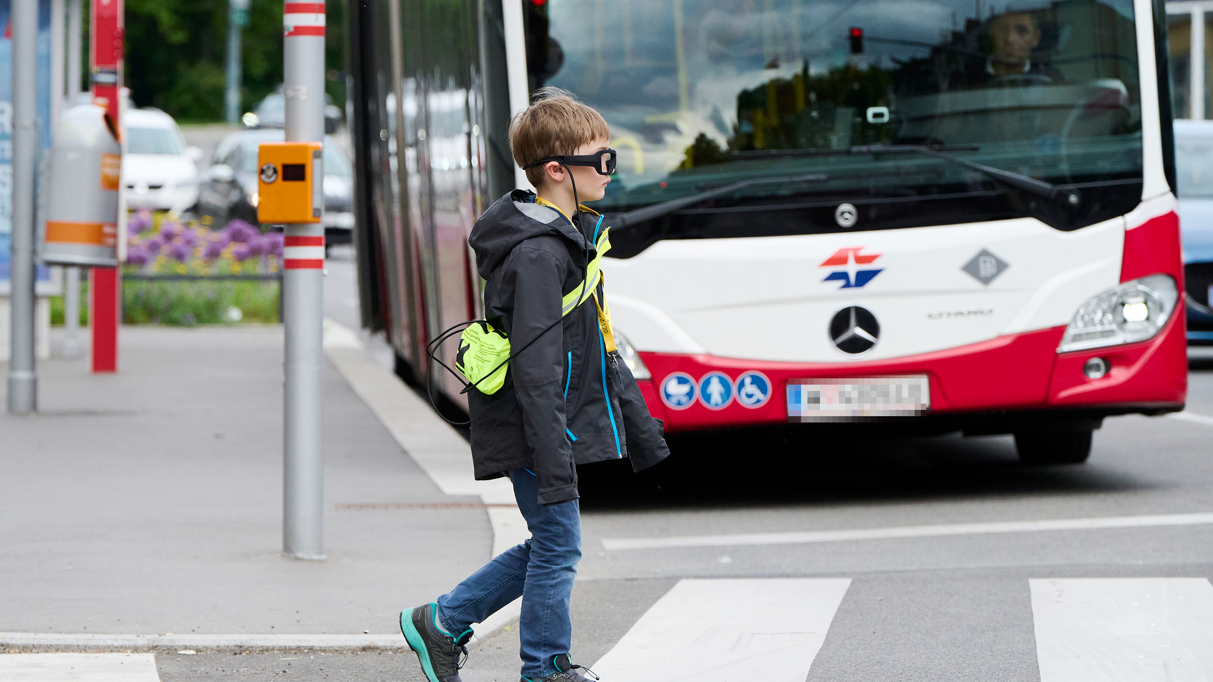 Ein Kind mit einer Blickbewegungsbrille überquert die Straße. Im Hintergrund sieht man einen Autobus.