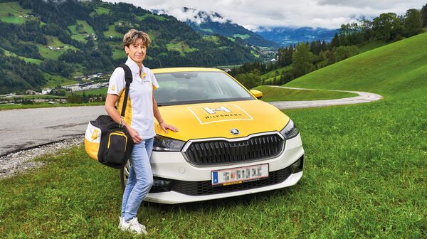 Hauskrankenpflegerin Heidi posiert vor ihrem Auto in den Bergen.