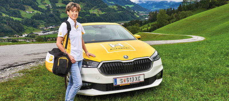 Hauskrankenpflegerin Heidi posiert vor ihrem Auto in den Bergen.