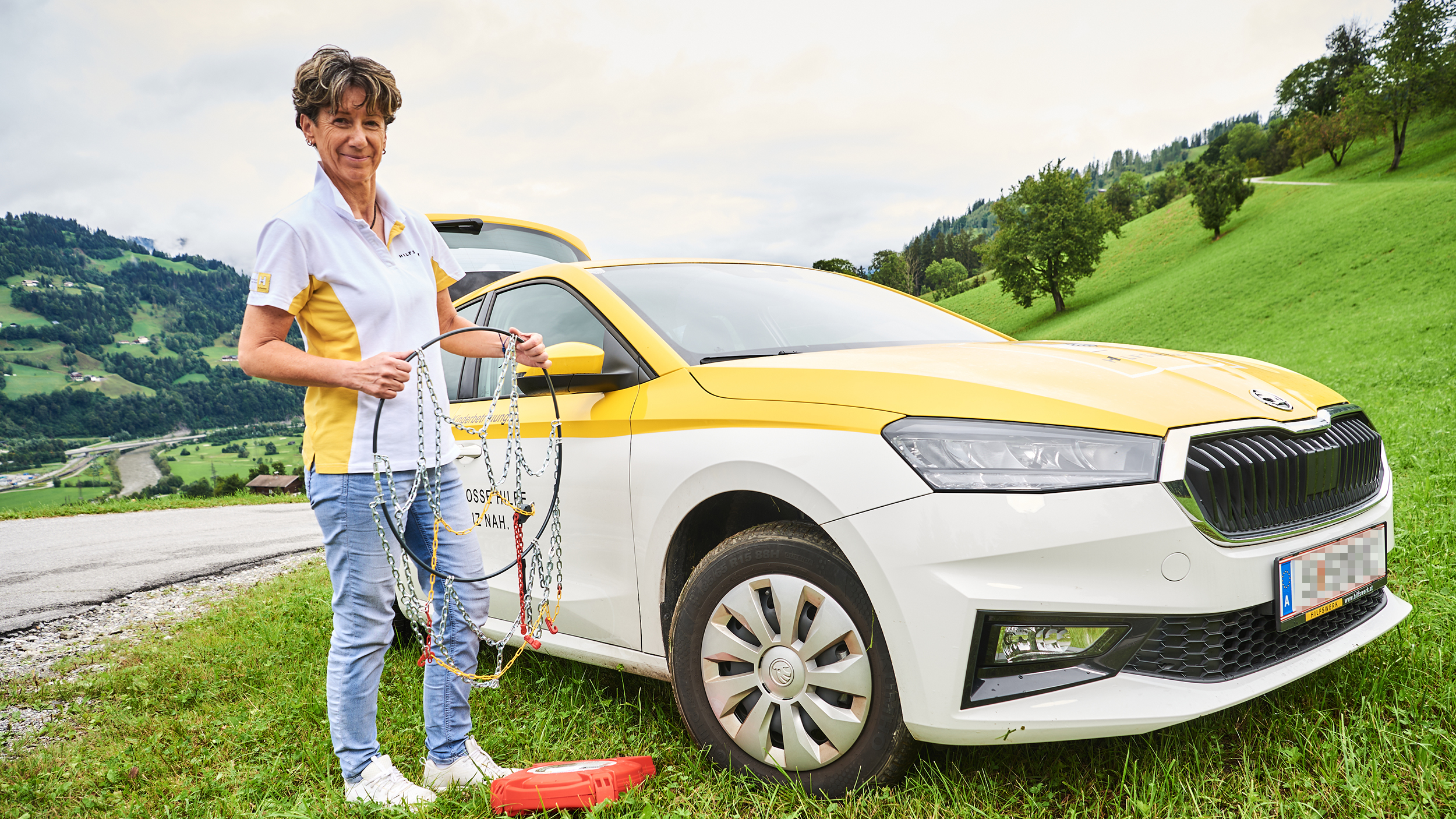 Hauskrankenpflegerin Heidi Aschacher steht vor ihrem Auto und hält fürs Foto Schneeketten in der Hand.