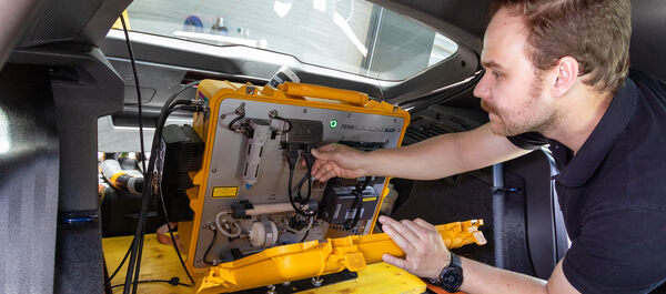 Ein Techniker arbeitet an einem mobilen Abgasmessgerät im Kofferraum eines Autos.