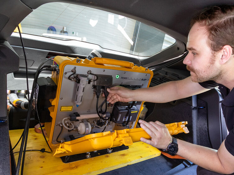 Audi A3_PEMS_Mai24_HE_007.jpg Ein Techniker arbeitet an einem mobilen Abgasmessgerät im Kofferraum eines Autos.