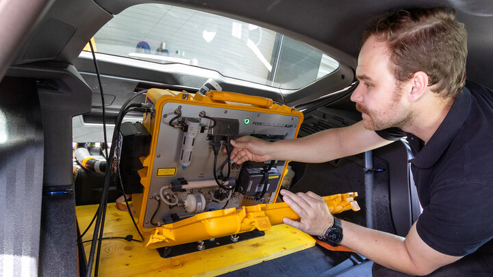 Ein Techniker arbeitet an einem mobilen Abgasmessgerät im Kofferraum eines Autos.