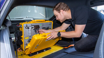 Dominik Darnhofer und das PEMS. Ein Techniker arbeitet an einem mobilen Abgasmessgerät im Kofferraum eines Autos.
