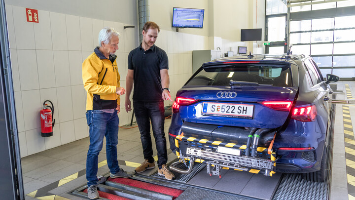 auto touring-Redakteur Günter Rauecker (links) und ÖAMTC-Techniker Dominik Darnhofer. Zwei Personen stehen neben dem Heck von einem blauen Auto, an dessen Heck ein mobiles Abgasmessgerät montiert ist.