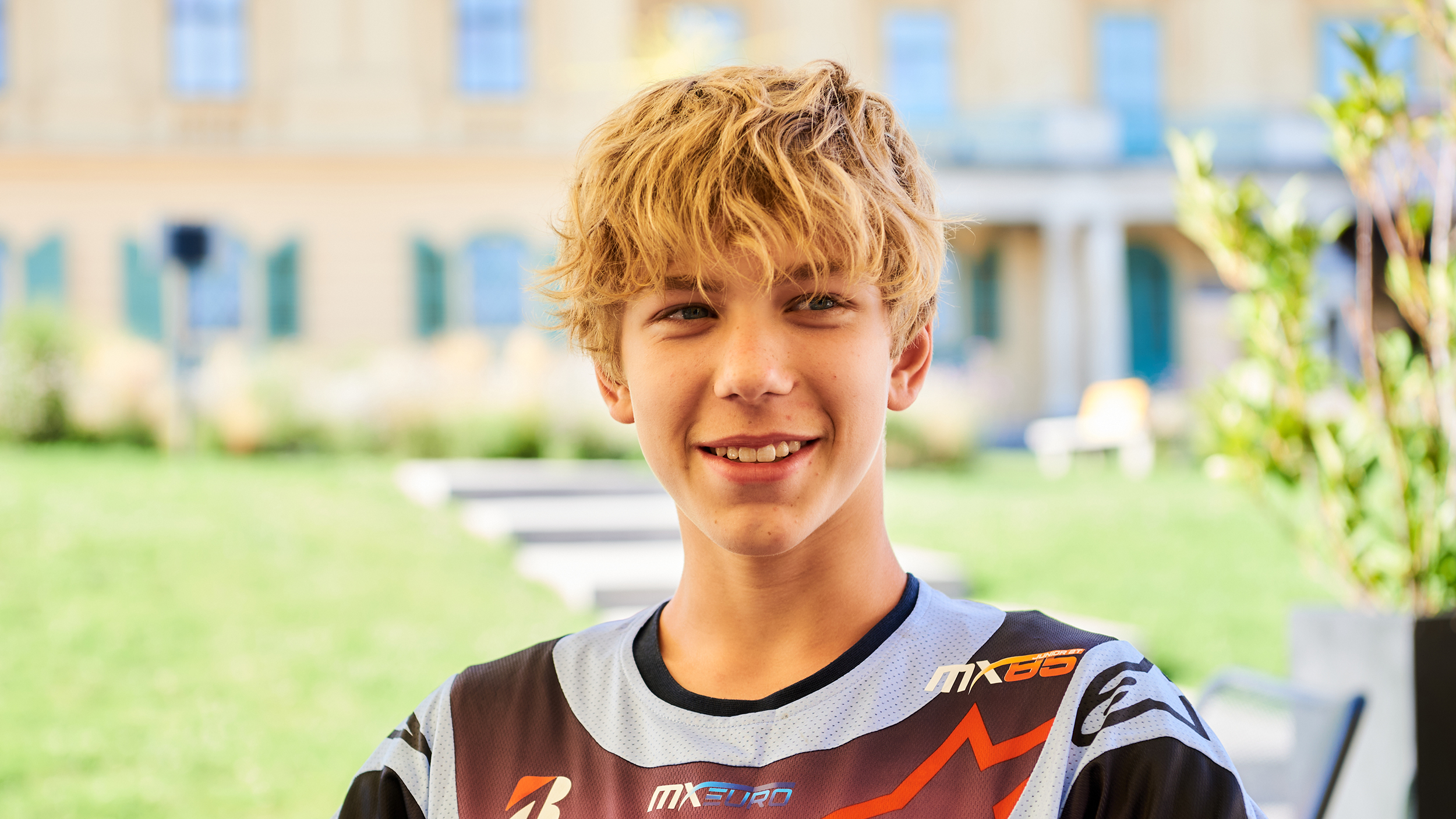 Ein junger Motorcross-Fahrer sitzt in einem Kaffee und lächelt. 