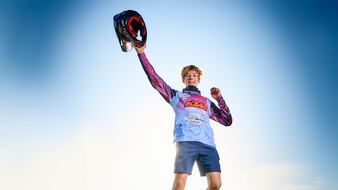 Ein junger Rennfahrer streckt stolz seinen Helm in die Luft.