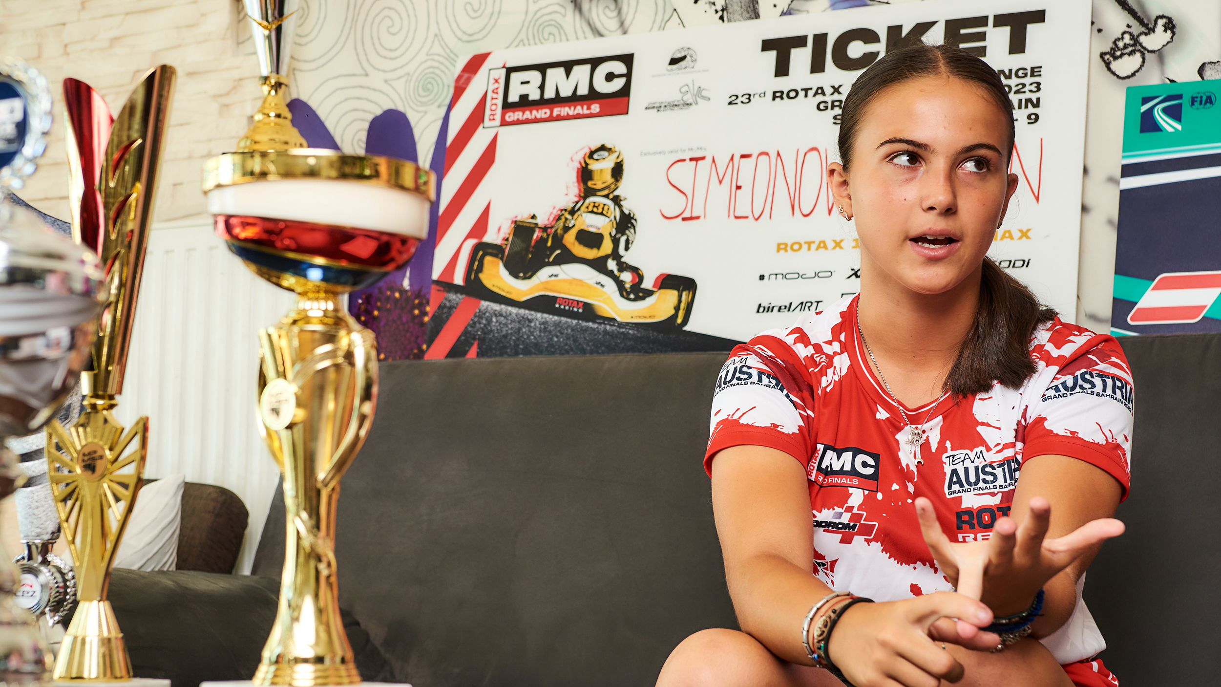 Eine junge Rennfahrerin sitzt auf einer grauen Couch und gestikuliert.