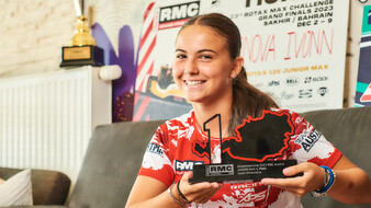 Eine junge Motorsportlerin präsentiert einen Pokal, der die Form von Österreich hat.