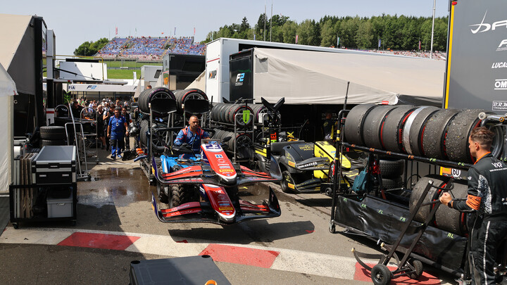 Mechaniker schieben Frontflügel und Reifen von Formel-Rennautos durch ein Fahrerlager.