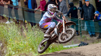 Ein Motocross-Rennfahrer springt mit seinem Motorrad über eine Kuppe.