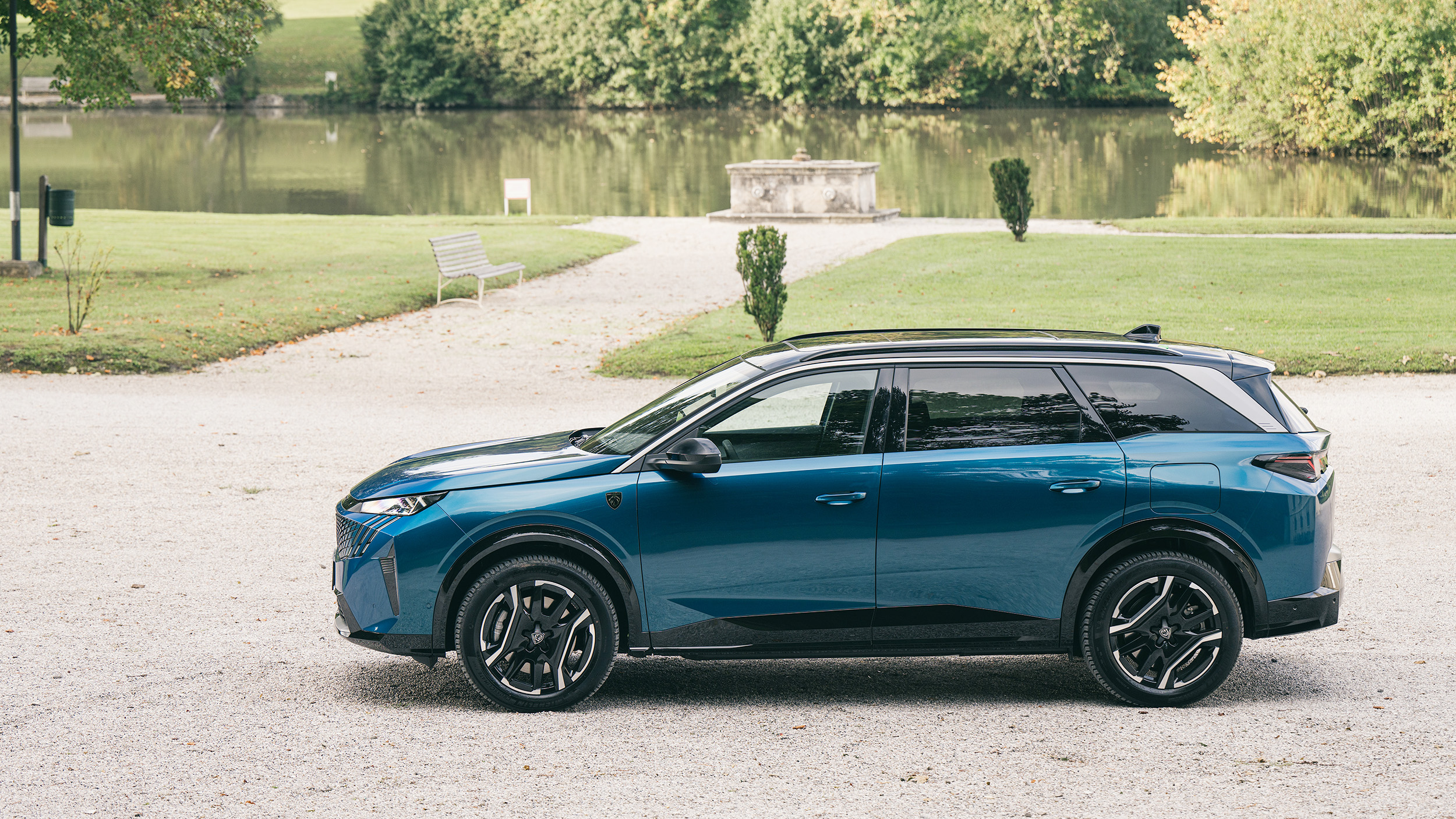 Ein blaues SUV steht in einem Park vor einem Teich