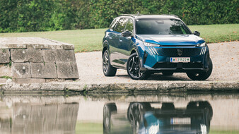 Blaues SUV steht vor einem Teich und spiegelt sich darin