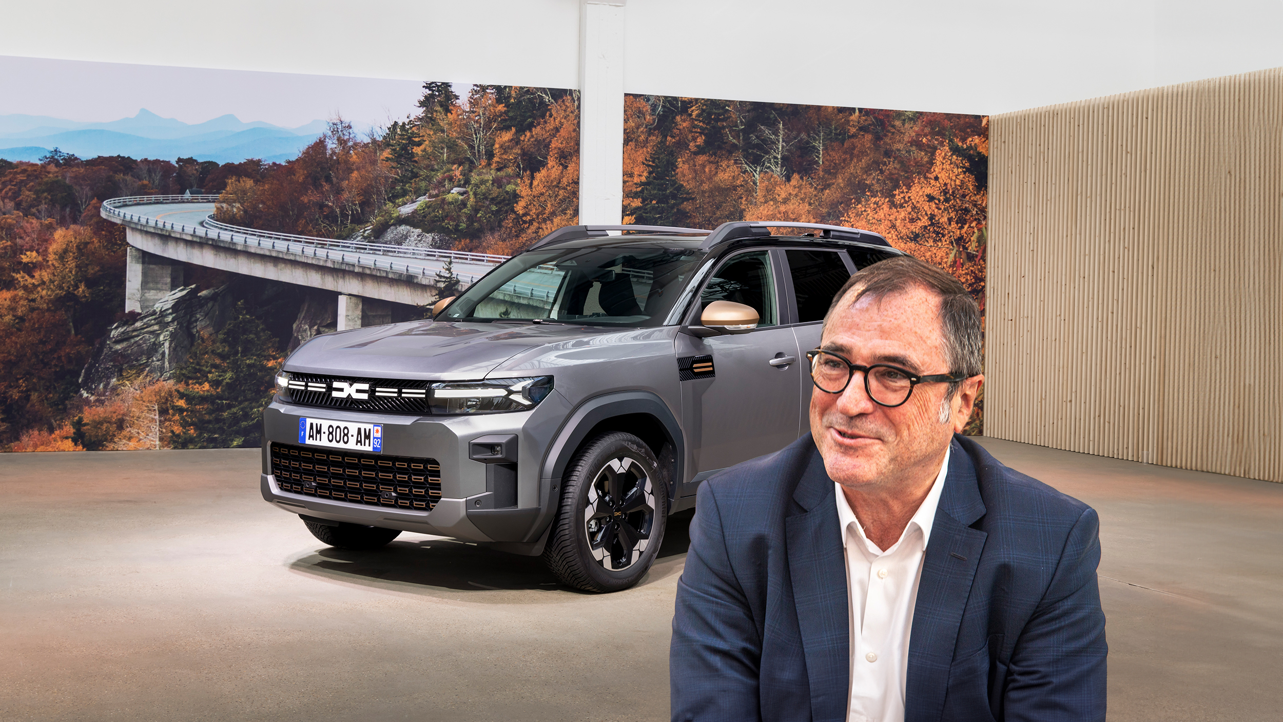 Dacia-CEO Denis Le Vot. Im Hintergrund steht ein graues SUV in einem Studio.