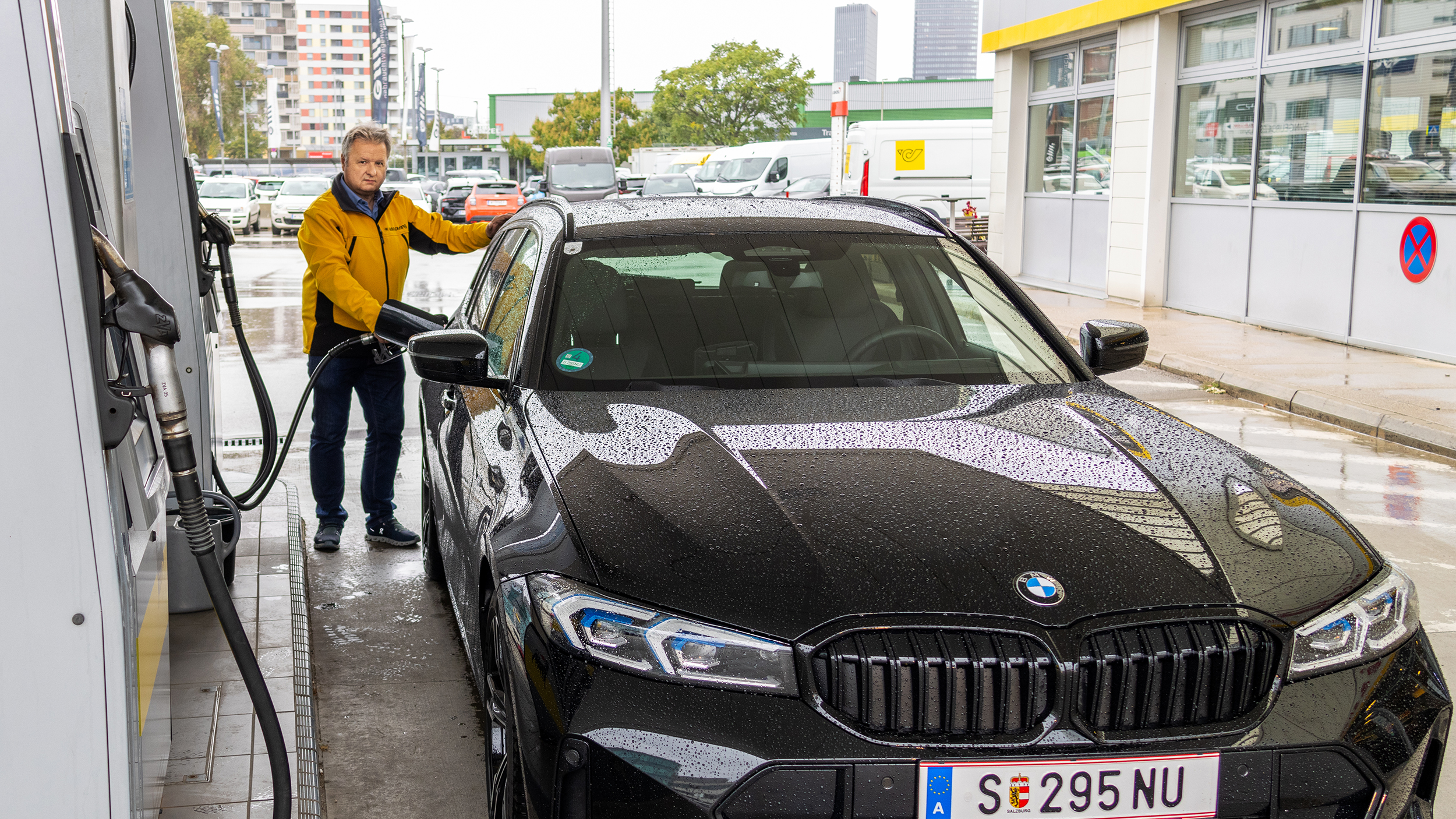 Ein Mann in gelber Jacke betankt ein schwarzes Auto
