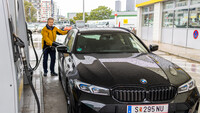 Ein Mann in gelber Jacke betankt ein schwarzes Auto