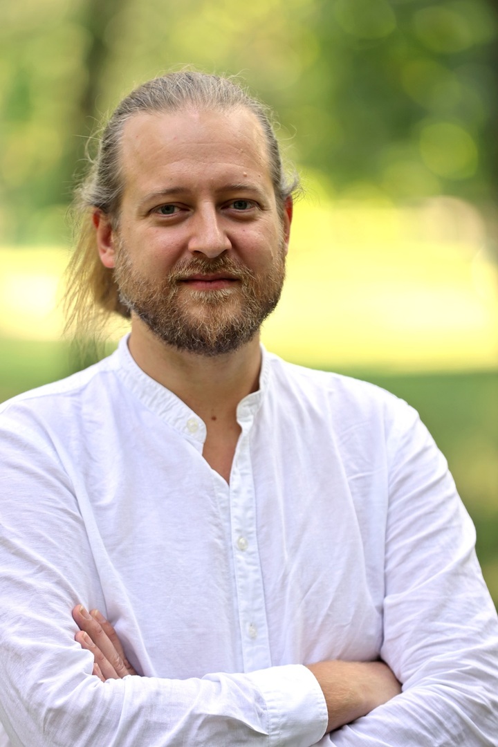 Das Bild ist ein Portraitfoto von Michael Szemes. Er trägt ein weißes Hemd und verschränkt die Arme. Der Hintergrund ist grün.
