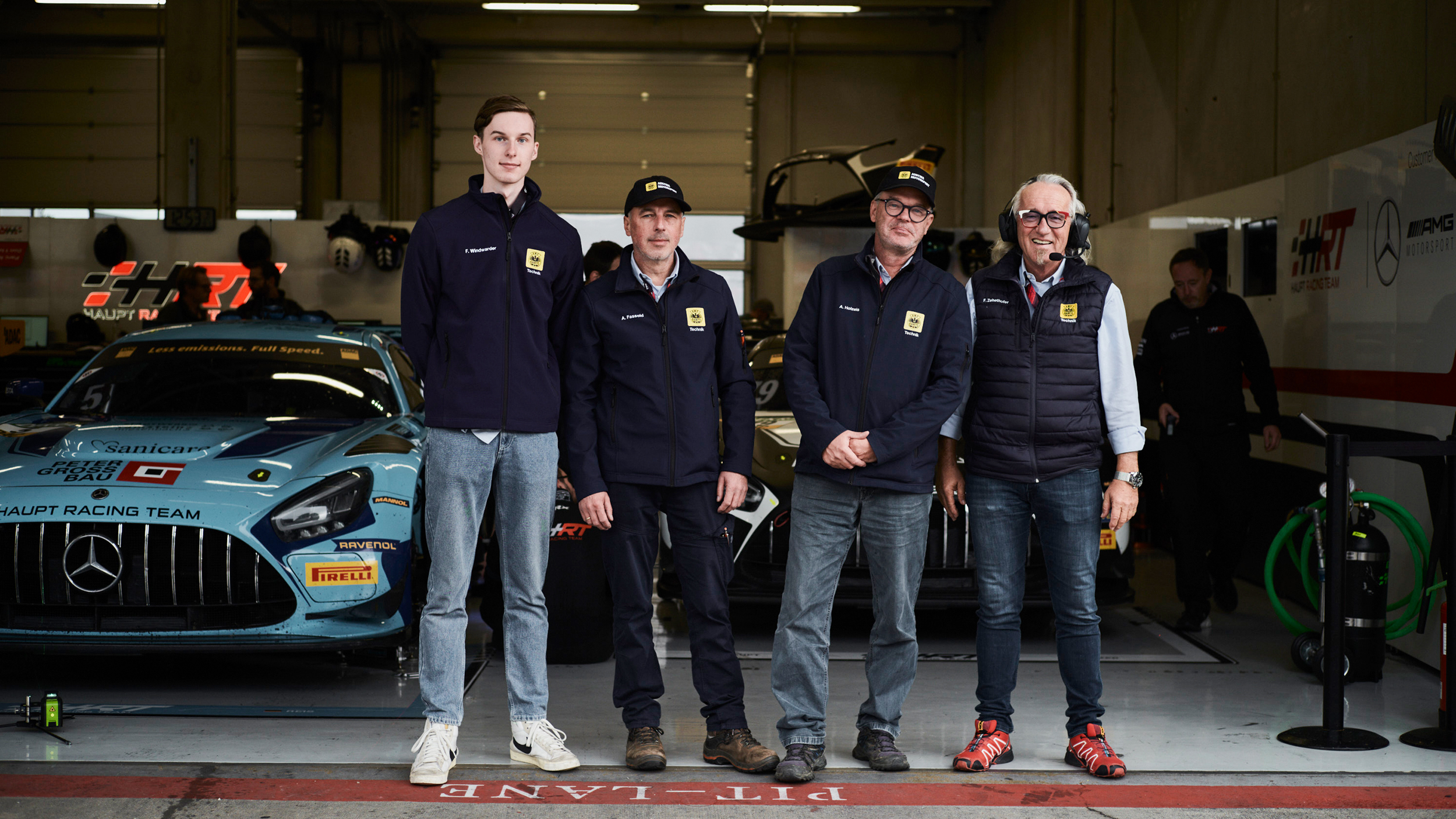 Vier technische Kommissare stehen vor einer Box am Red Bull Ring, im Hintergrund ist ein Rennauto zu sehen.