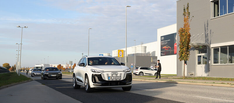 Ein weißer Audi fährt an einem grauen Gebäude vorbei