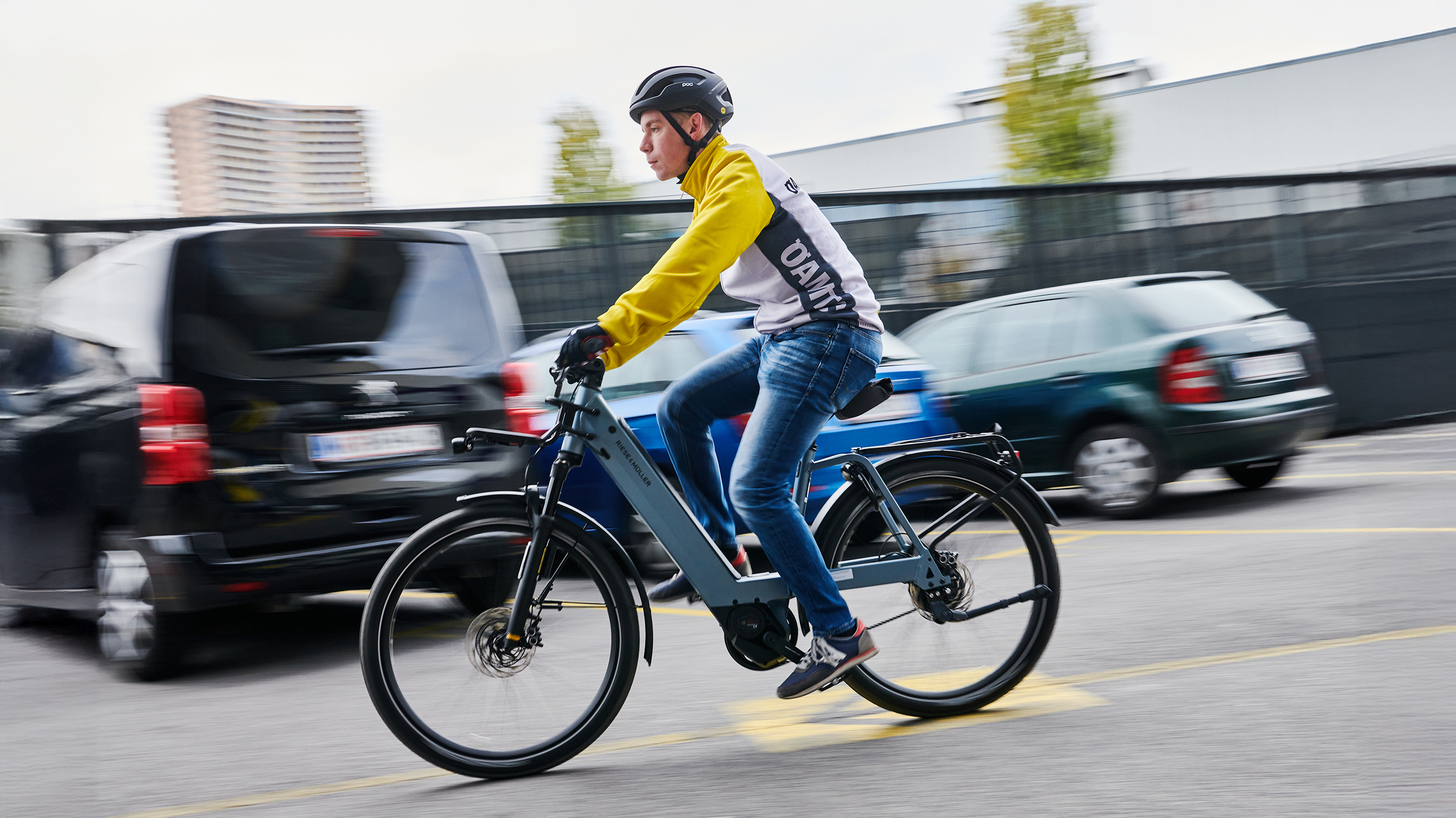 Ein Mann in gelber Jacke fährt am Fahrrad an Autos vorbei