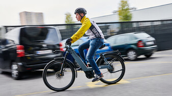 Ein Mann in gelber Jacke fährt am Fahrrad an Autos vorbei