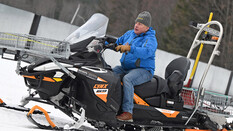 Ein Mann fährt auf eine Ski-Doo im Hintergrund Wälder.