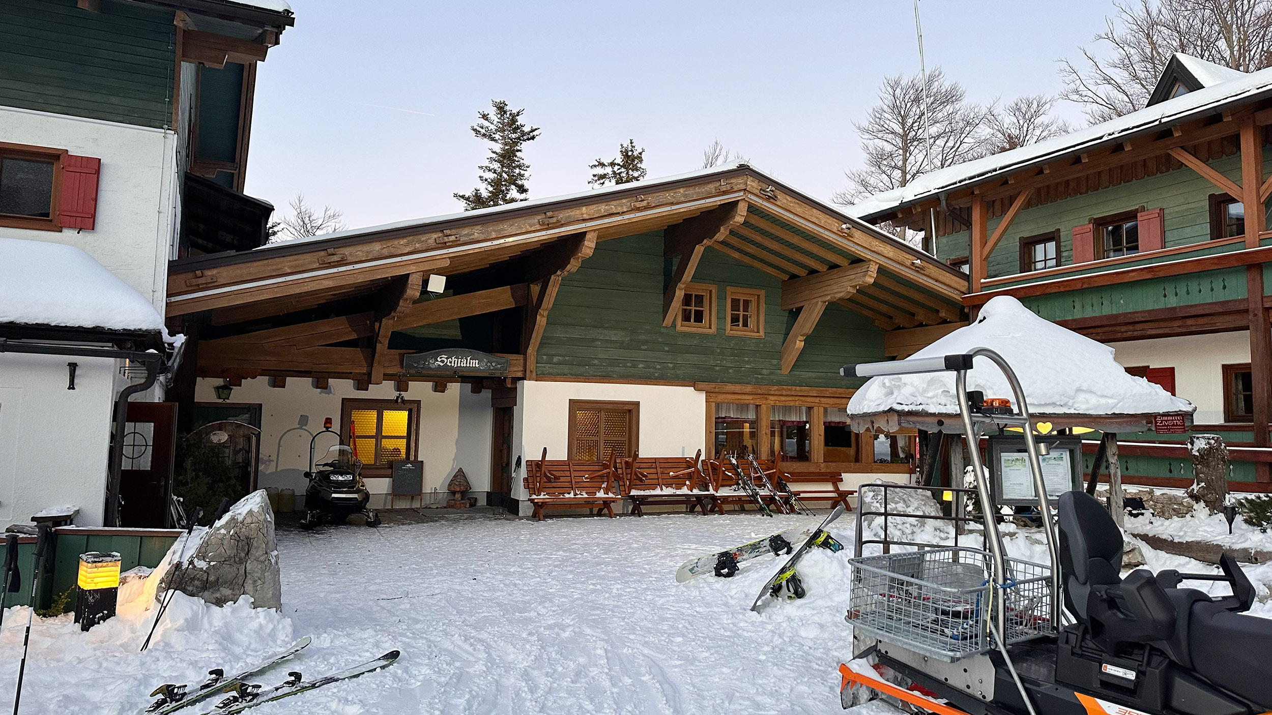 Außenaufnahme des Hotels Hochberghaus am Kasberg in Grünau im Almtal. Zu sehen sind drei Gebäude, davor liegen Ski im Schnee.
