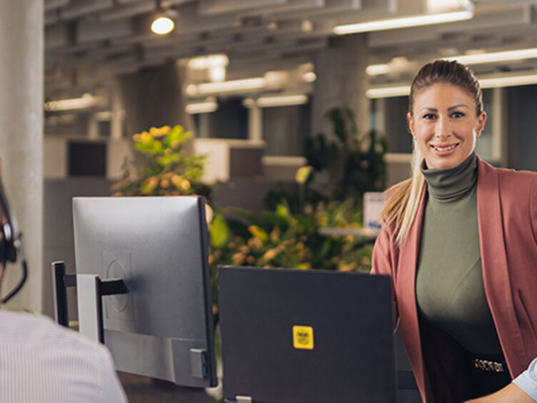 In der ÖAMTC Einsatzzentrale: Drei männliche und zwei weibliche Personen. Drei Personen sitzen mit Headsets am Kopf und haben Bildschirm oder Laptop vor sich. Zwei Personen unterhalten sich stehend.