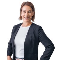 Frau mit kinnlangem, braunen Haar lächelt in die Kamera. Sie trägt einen schwarzen Blazer und ein weißes T-Shirt.