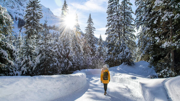 Eine Frau in einem gelben Anorak spaziert durch einen verschneiten Wald.
