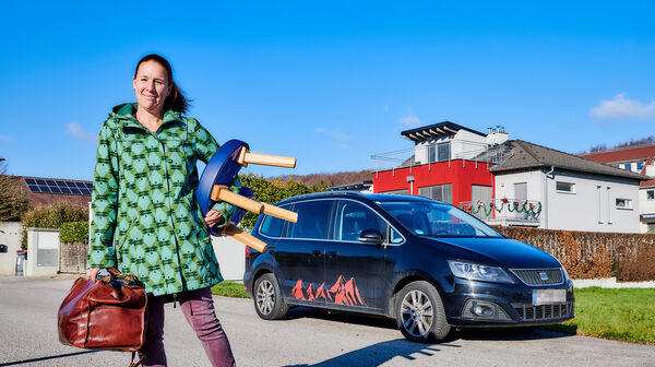 Hebamme Martina Klasz hält ihr Arbeitsgerät: Gebärstuhl und Tasche in der Hand und steht vor ihrem Auto.