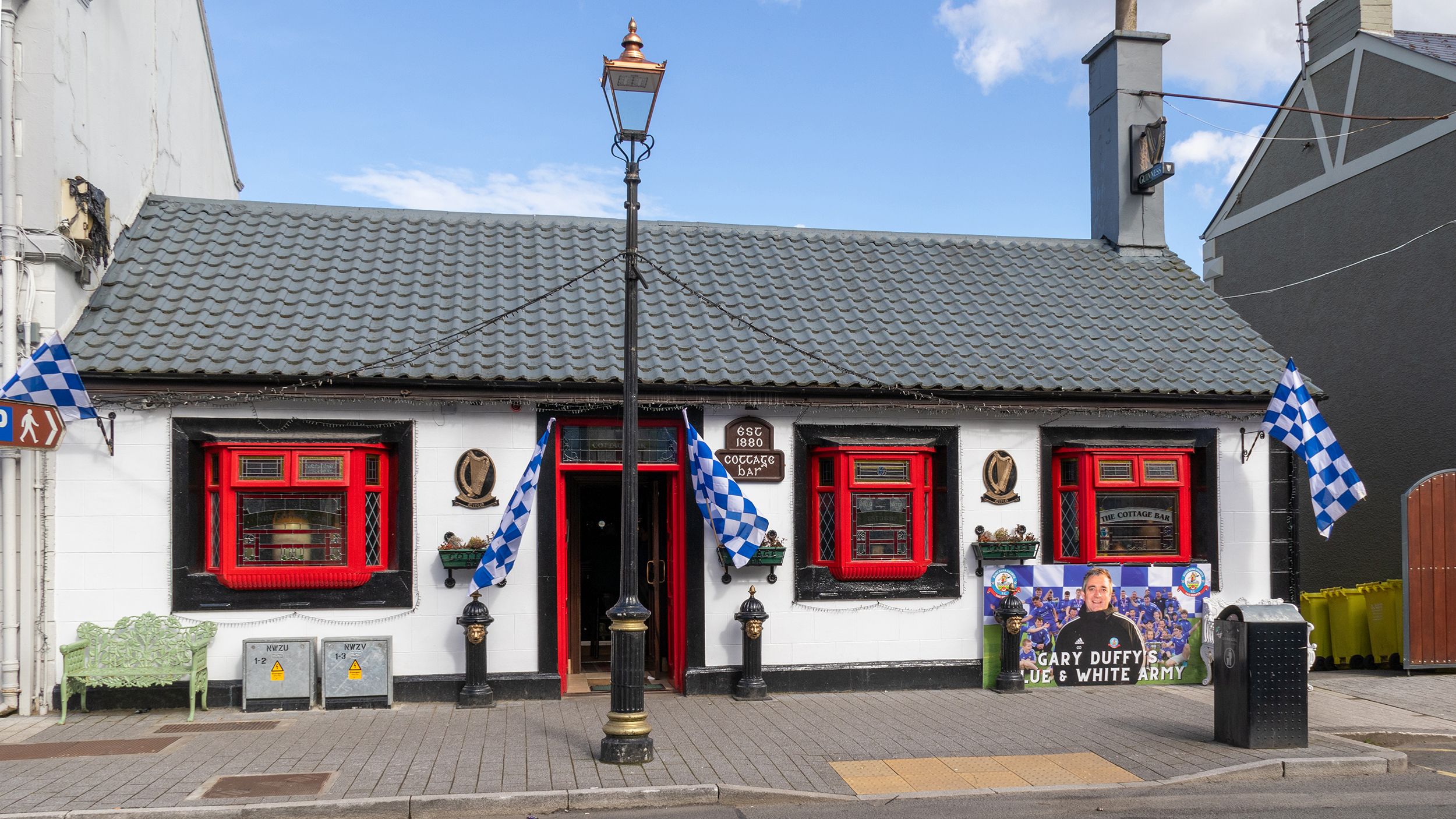 Irisches Pub mit roten Fensterrahmen und blau-weiß karierten Fanclub-Fahnen.