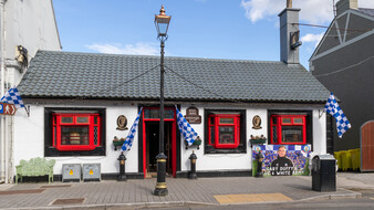 Irisches Pub mit roten Fensterrahmen und blau-weiß karierten Fanclub-Fahnen.