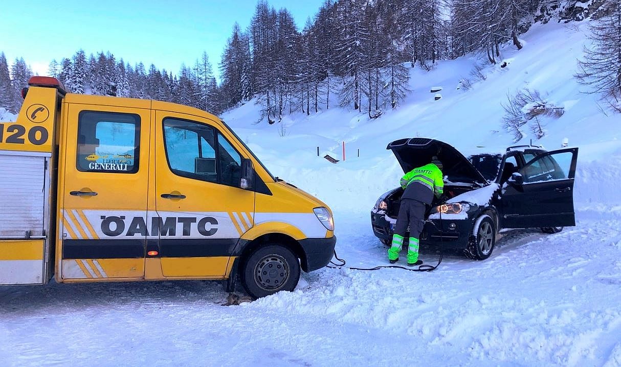 ÖAMTC Pannenfahrzeug auf verschneiter Straße, Pannenfahrer gibt einem Auto Starthilfe.