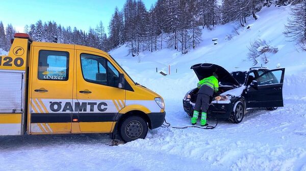 ÖAMTC Pannenfahrzeug auf verschneiter Straße, Pannenfahrer gibt einem Auto Starthilfe.