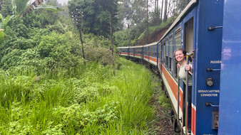 Bild von einem fahrenden Zug von außen, aus einer Zugtür fotografiert. Redakteurin Verena Schauer schaut lächelnd aus einer anderen Zugtür.