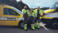 Zwei männliche und eine weibliche Pannenhelfer_innen stehen vor ihren Fahrzeugen.