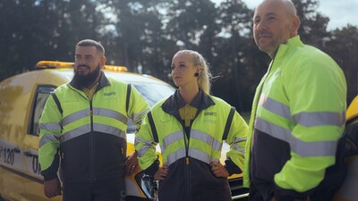 Zwei männliche und eine weibliche Pannenhelfer_innen stehen vor ihren Fahrzeugen.