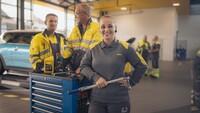 Zwei männliche und eine weibliche Kfz-Technikerin stehen an einer Werkbank in der Kfz-Technik Werkstatt.