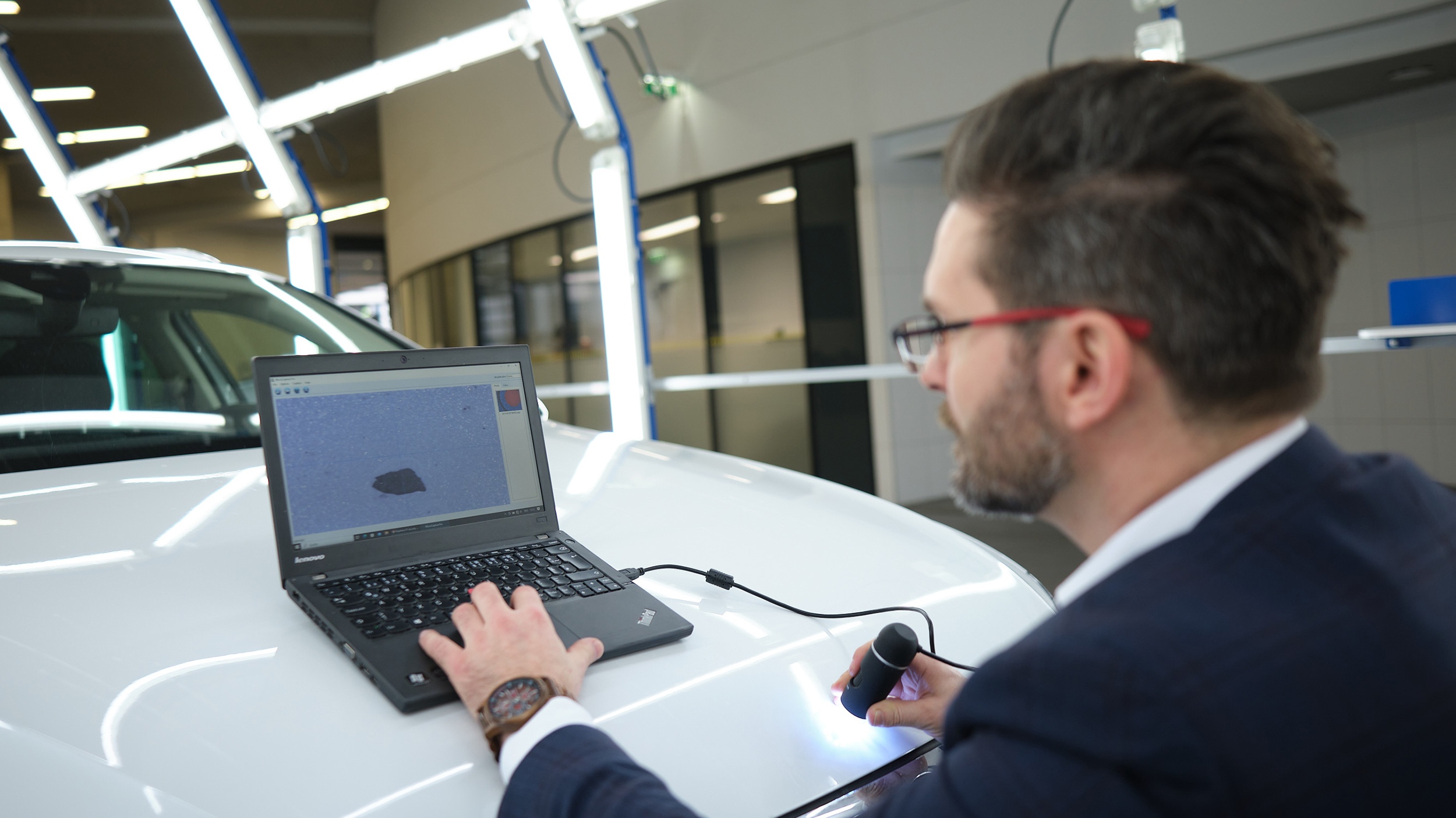 Michael Planer kontrolliert mit einem Laptop die Motorhaube eines Autos