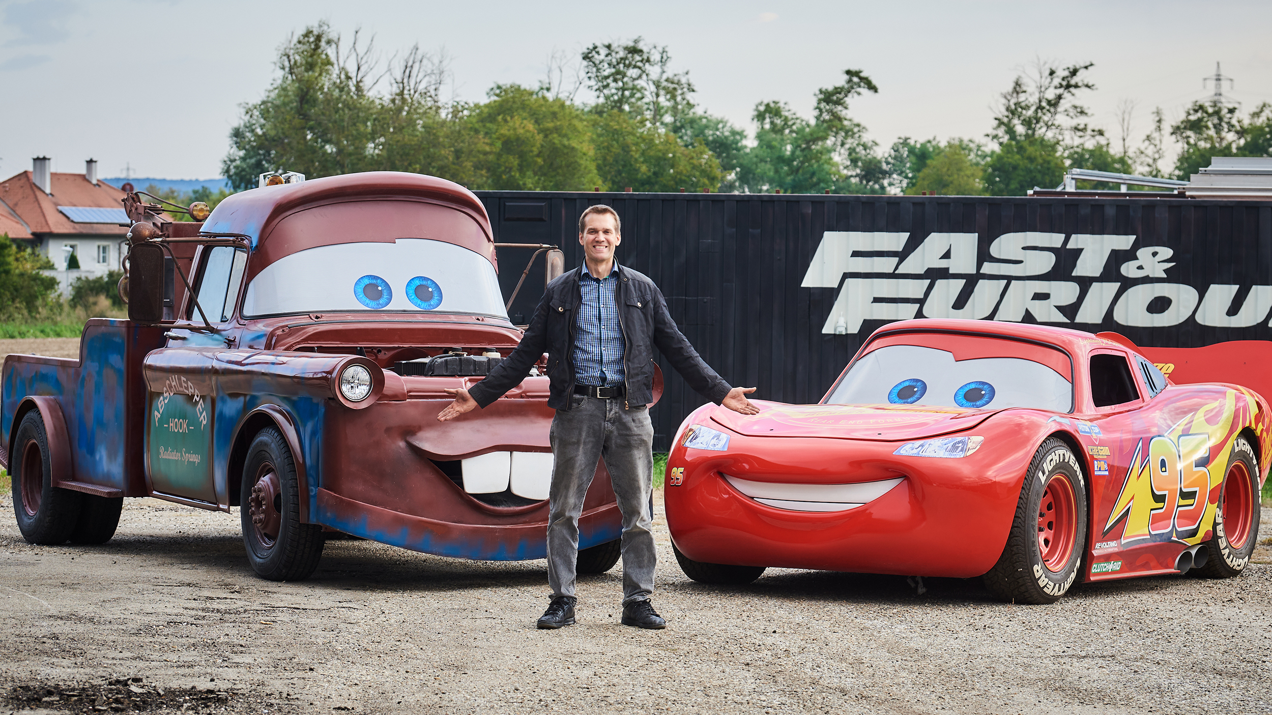 Martin Hahn steht vor den Filmautos aus Cars, Lightning McQueen (links) und Hook (rechts)