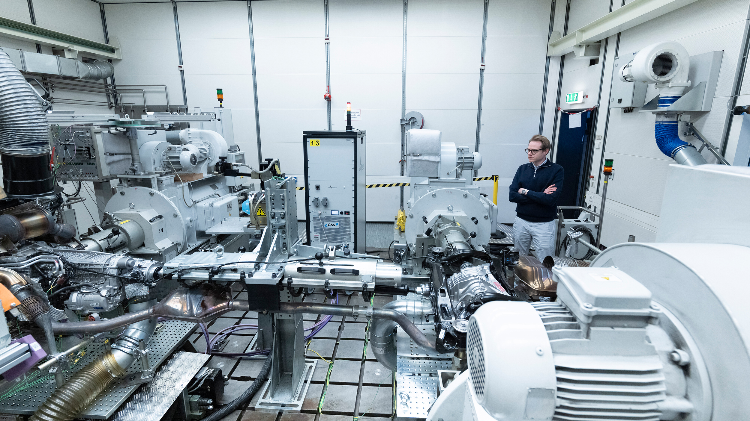 Eine Person steht in einem Prüfstand-Raum und sieht sich mit verschränkten Armen die Technik an.