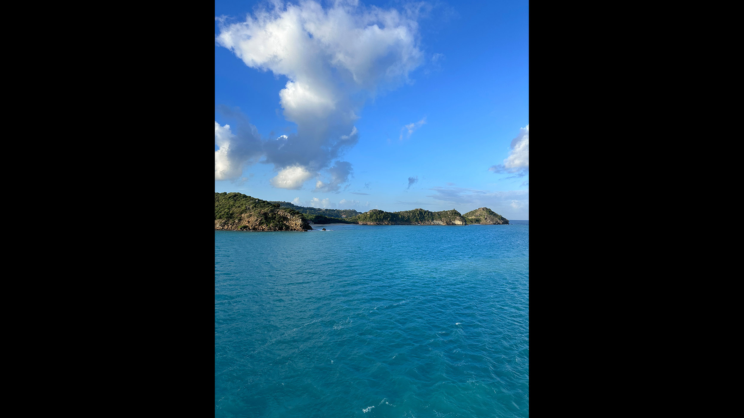 Blick vom Meer auf eine Küstenlandschaft bei strahlendem Wetter mit blauem Himmel.